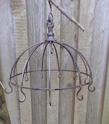 A rustic metal hanging basket with hooks, suspended from a branch against a wooden fence.
