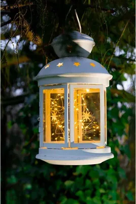 A white lantern with fairy lights inside hangs from a tree branch.