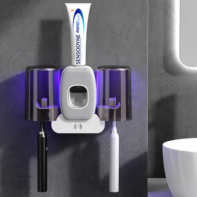 A bathroom accessory set mounted on a wall, featuring a toothpaste dispenser and two toothbrush holders with UV lights.