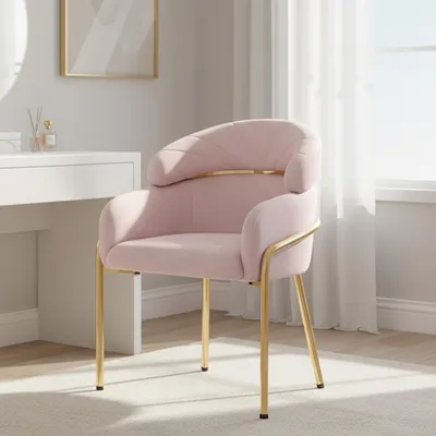 A pink upholstered chair with gold metal legs is shown in a well-lit room, possibly a bedroom or dressing area, next to a white vanity table.
