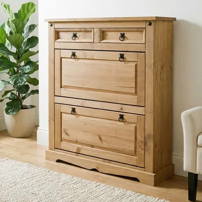 A wooden shoe cabinet with two flip-down doors and two drawers, placed in a room with a potted plant and a rug.