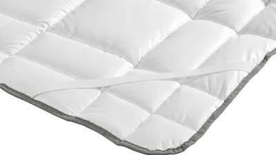 A close-up, angled view of a white quilted mattress topper with a gray border and elastic straps.