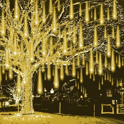 A tree decorated with yellow LED lights that resemble meteor showers, set against a dark background with buildings in the distance.
