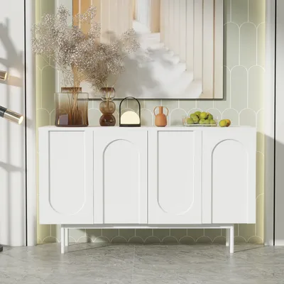 A white sideboard with decorative arched doors is displayed in a room with light green scalloped wallpaper and a large abstract painting above it.