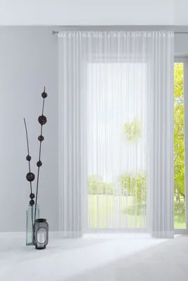 A sheer white curtain hangs in front of a window, with a decorative branch in a vase and a lantern on the floor in the foreground.
