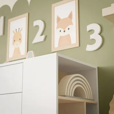 A close-up view of a white dresser with framed animal art and wooden numbers on a green wall.