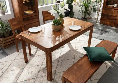 A wooden dining table and bench set in a well-lit room with plants.