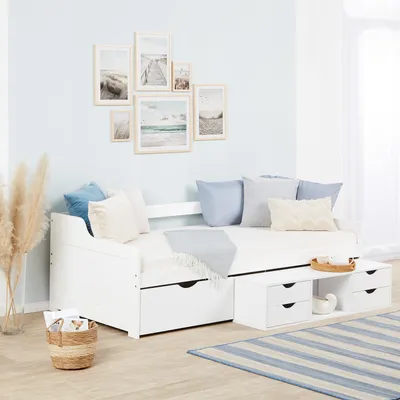 A white daybed with drawers is set up in a room with light blue walls and beach-themed artwork.