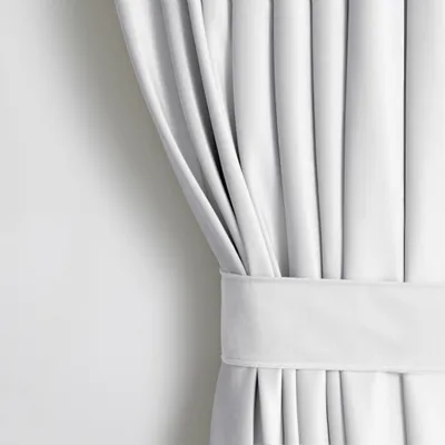 A close-up view of a white curtain with pleats and a fabric band.