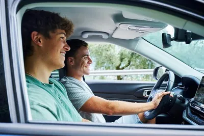 Two young men are smiling and looking forward while sitting in a car.