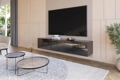 A modern living room with a large TV mounted on the wall above a sleek, black TV stand. Two coffee tables are placed in front of the stand on a light-colored rug. A chair and a plant are also visible in the scene.