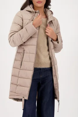A woman wearing a beige puffer coat and dark blue jeans against a white background.