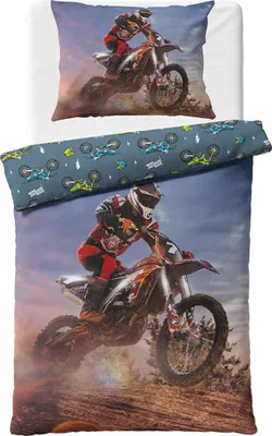 A motocross rider in action on a dirt bike, with a pillowcase and duvet cover featuring similar designs.