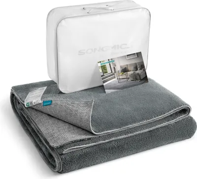 A folded gray rug is displayed in front of its white packaging bag, with a small marketing card leaning against the bag.