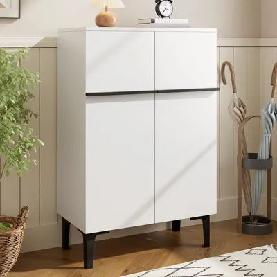 A white cabinet with black legs and handles, placed in a room with wooden floors and a wall paneling.