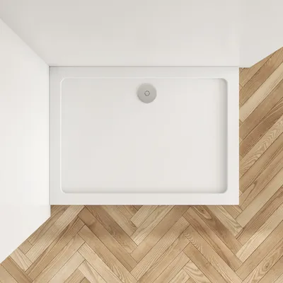 A top-down view of a white rectangular shower tray on a herringbone wooden floor.