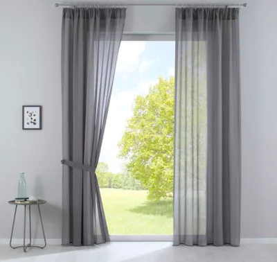 A window with gray sheer curtains, showing a green tree and blue sky outside.