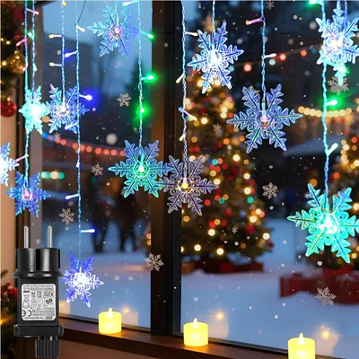 Christmas lights in the shape of snowflakes hanging in a window with a Christmas tree in the background.