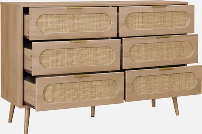 A wooden dresser with six drawers, each featuring a rattan insert and a gold handle, set against a plain white background.