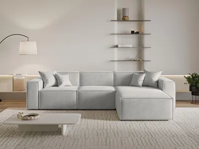 A modern living room with a light gray sectional sofa, a white coffee table, and shelves on the wall.