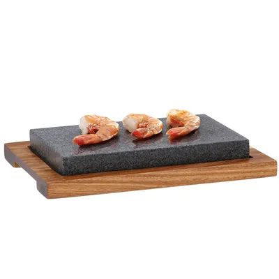 A serving stone with three shrimp on it, placed on a wooden base.