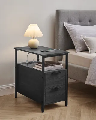A bedside table with drawers and a lamp next to a bed.