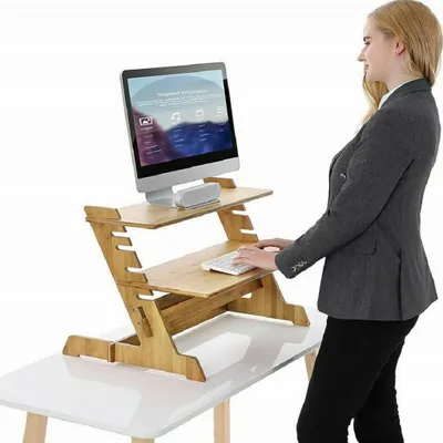 A woman is using a standing desk converter made of bamboo, which is placed on top of a white desk.