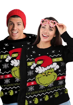 A man and a woman wearing matching Grinch-themed Christmas sweaters against a white background.