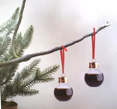 Two clear, fillable Christmas ornaments shaped like lightbulbs hang from a branch, filled with a dark liquid.