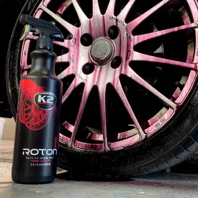 A bottle of K2 Roton Pro wheel cleaner is shown next to a car wheel that has been sprayed with the product, causing it to turn purple.
