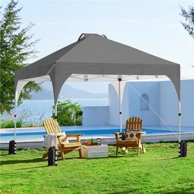 A pop-up canopy tent set up on a lawn next to a swimming pool, with two chairs and a table.