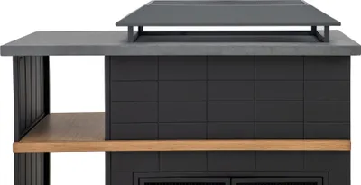 A close-up view of a black outdoor fireplace with a gray stone countertop and a wooden shelf.