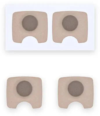 Languettes adhésives beiges Resty Magnetic : une paire sur son film protecteur et deux languettes détachées, chacune avec un disque rond foncé et une encoche d'un côté, sur fond blanc.