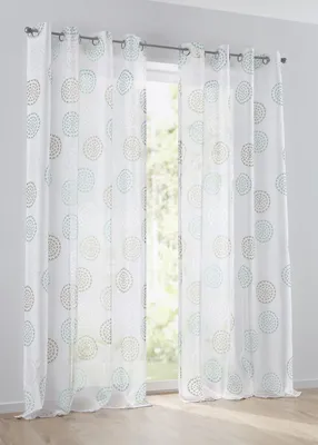 Two white sheer curtains with a circular pattern are hanging in front of a window.