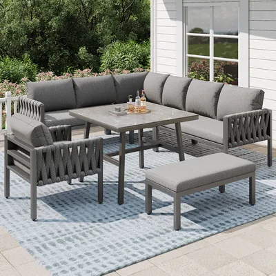An outdoor patio set with a sectional sofa, table, and bench on a rug.