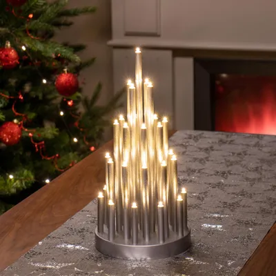 A decorative LED candle pyramid is placed on a table next to a Christmas tree and a fireplace.