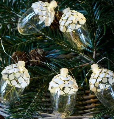 Acorn-shaped LED lights are strung together and intertwined with evergreen branches and pinecones.