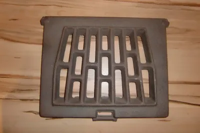 A cast iron grate for a stove or fireplace is shown on a wooden surface.