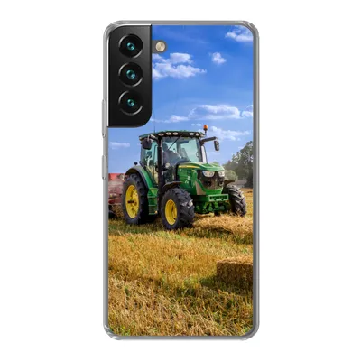 A green tractor in a field of hay under a blue sky.