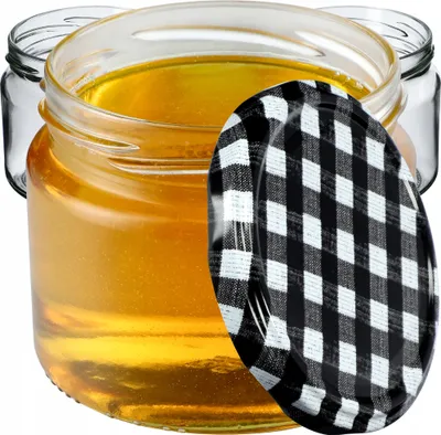 A close-up of a glass jar filled with honey, with a black and white checkered lid partially obscuring the jar.