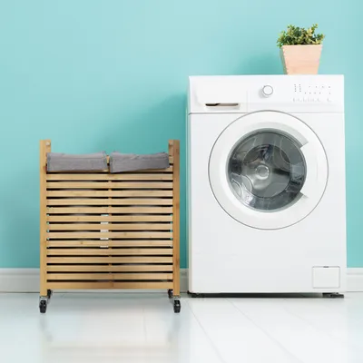 A laundry basket and washing machine are shown against a light blue wall.