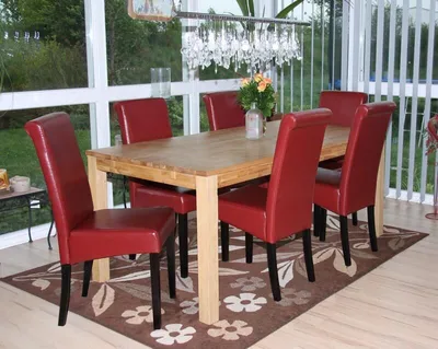 A dining room with a wooden table and six red chairs, set in a sunroom with large windows.