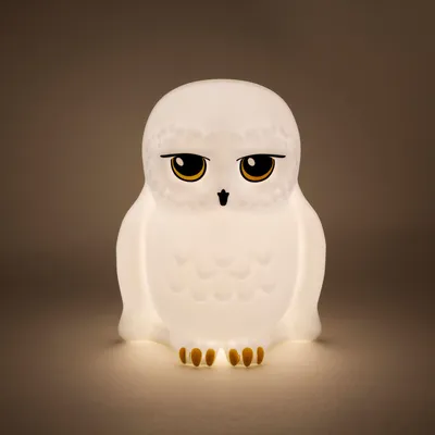 A white owl lamp with yellow eyes and black accents, lit from within, sits on a neutral background.