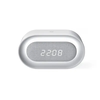 A white, oval-shaped digital alarm clock with a gray fabric speaker grille displaying the time.