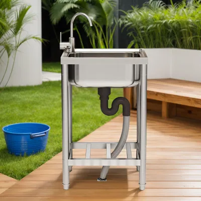An outdoor sink setup with a blue bucket on grass and a wooden deck.