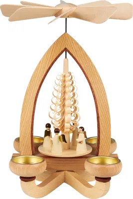 Auf dem Bild ist eine kunstvoll gestaltete Weihnachtspyramide aus Holz zu sehen die mit einem filigranen Propeller und vier Kerzenhaltern ausgestattet ist und in der Mitte eine kleine Szene mit Figuren und einem spiralförmigen Baum zeigt