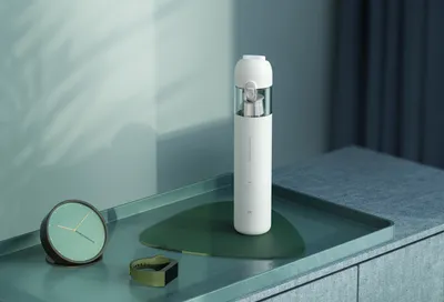 A white Xiaomi vacuum cleaner is placed on a tray with a clock and a watch.