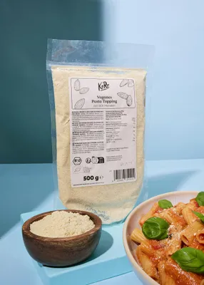 A bag of vegan pasta topping and a bowl of the topping are shown next to a bowl of pasta.