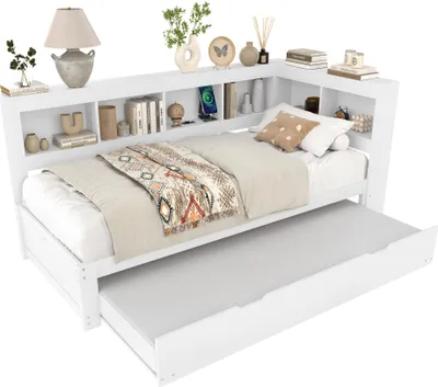 A white wooden bed with a pull-out trundle and a built-in bookshelf headboard, decorated with bedding and small decorative items.
