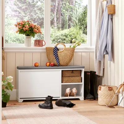 A hallway or entryway scene featuring a shoe cabinet with a bench seat, storage baskets, shoes, and decorative items.